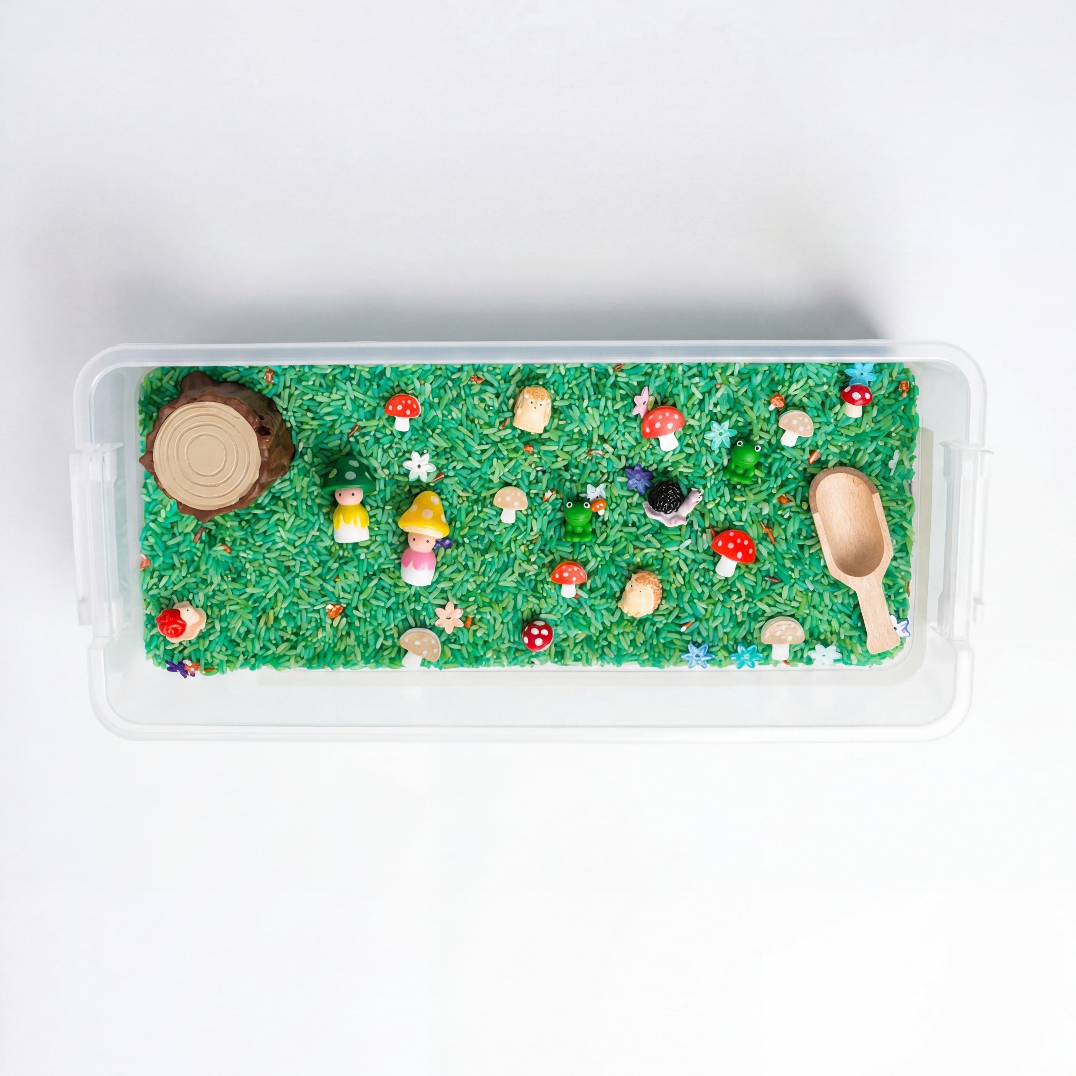 Children's sensory bin with green sand, wooden toys, and colorful decorations on a white background.